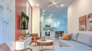 A modern living room with a sofa, armchairs, a coffee table, and a kitchen in the background.
