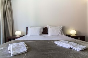 Een hotelkamer met een net opgemaakt bed, twee bedlampen en een set handdoeken op het bed.