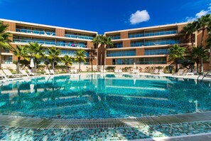 Een hotel met een groot zwembad, palmbomen en een moderne gevel.