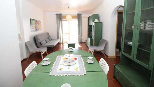 A dining area with a green table set for four, surrounded by white chairs. There is a green cabinet with glass doors to the right. - Refúgio da Falésia By D´alma Portuguesa (Albufeira)