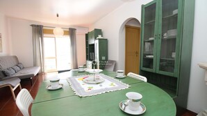 A dining area with a green table set for four, surrounded by white chairs. A green cabinet with glass doors is to the right. - Refúgio da Falésia By D´alma Portuguesa (Albufeira)