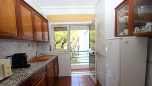 A compact kitchen with wooden cabinets, a white refrigerator, and a window overlooking a balcony. - Refúgio da Falésia By D´alma Portuguesa (Albufeira)