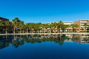 A hotel with a swimming pool, palm trees, and modern buildings.
