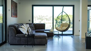 Un salon moderne avec un canapé d’angle gris, un fauteuil suspendu et une petite table ronde.