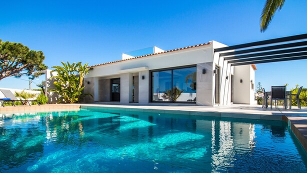 Une maison moderne dotée d’une piscine, de grandes fenêtres et d’un espace patio.
