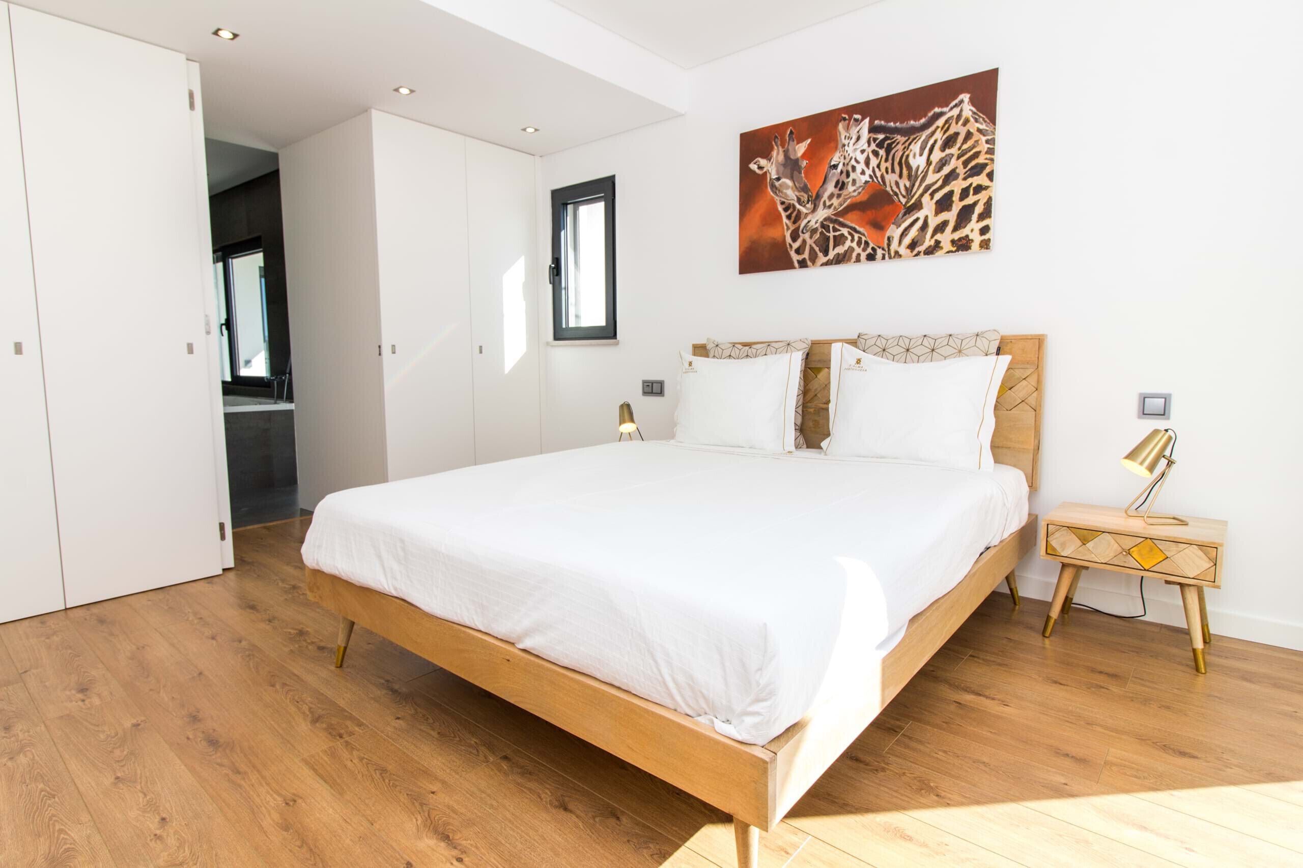 A modern bedroom with a wooden bed, white bedding, and a giraffe painting on the wall.