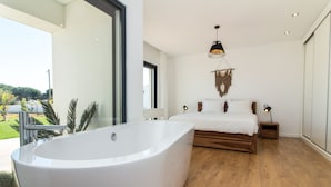 Une chambre moderne avec une grande baignoire, un lit en bois et une vue sur l’extérieur.