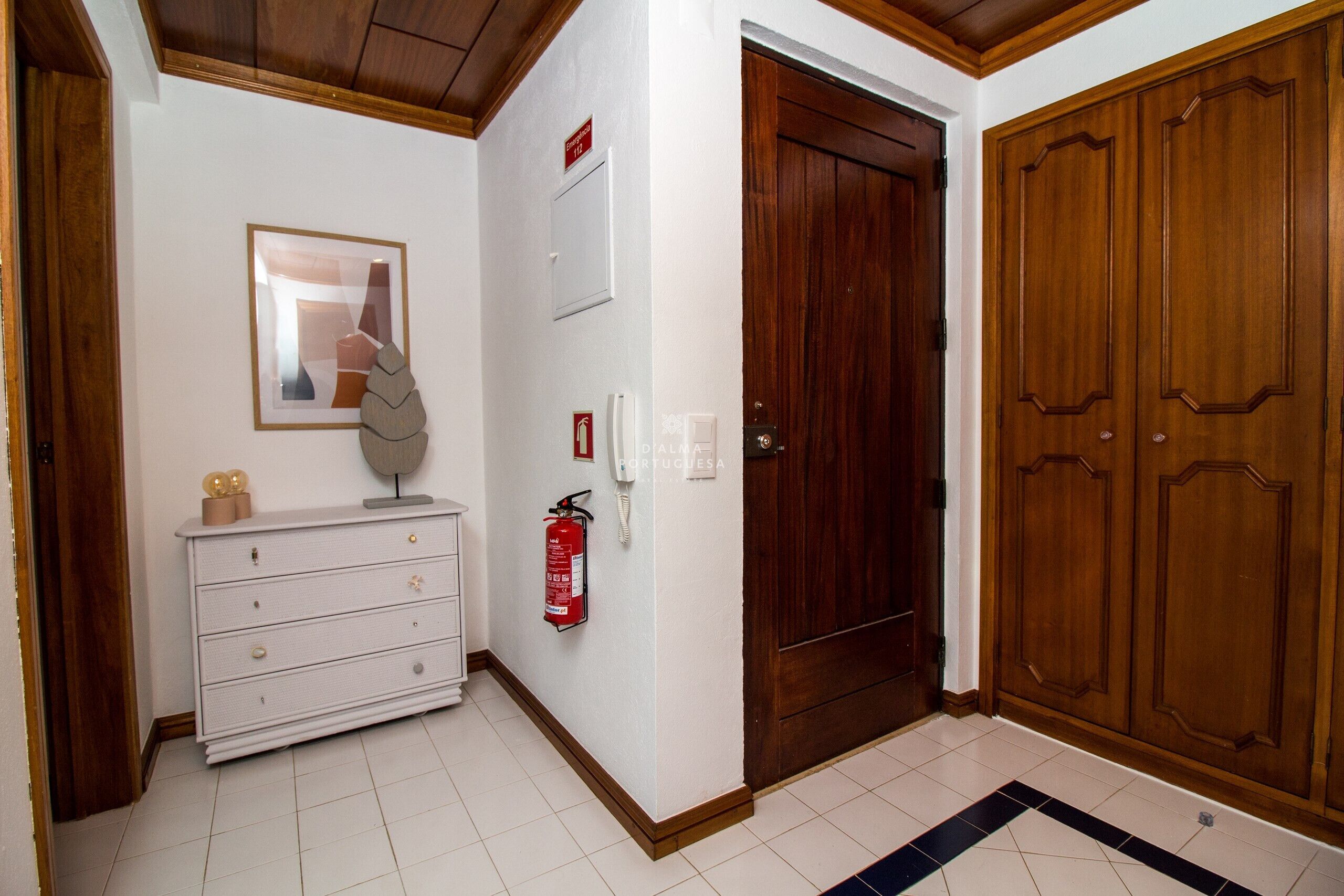 A hallway with a white dresser, a framed picture, a fire extinguisher, and a wooden door.