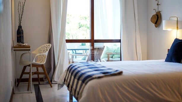 A bedroom with a bed, a chair, a table, and a window with curtains. - Salgados Lounge Dalma Portuguesa (Albufeira)