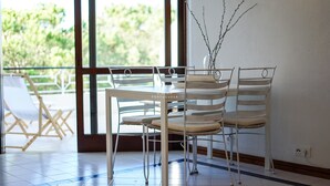 A dining area with a table and chairs, a vase with branches, and a view of greenery outside. - Salgados Lounge Dalma Portuguesa (Albufeira)