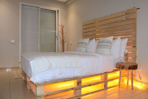 A bed with a wooden headboard, white bedding, and a small wooden table beside it. - Stylish Wooden Apartment with Pool (Agadir)