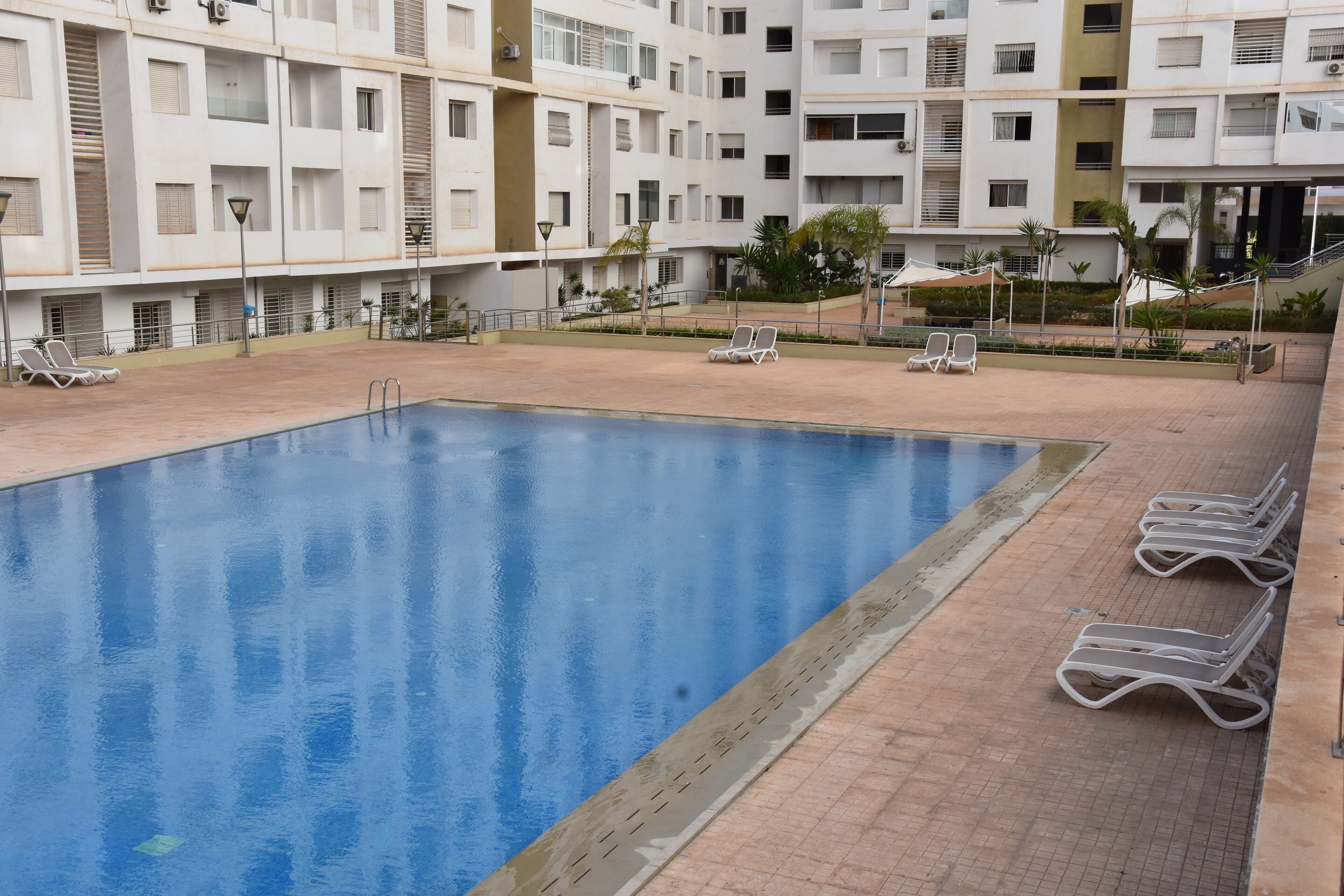 A swimming pool with lounge chairs and a building with multiple balconies in the background.