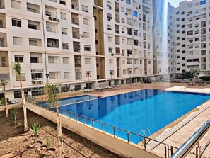Un immeuble d’appartements moderne doté d’une piscine centrale, entourée de chaises longues et d’un petit espace jardin.