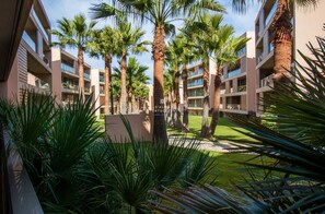 A hotel courtyard with palm trees, a lawn, and modern buildings with balconies.