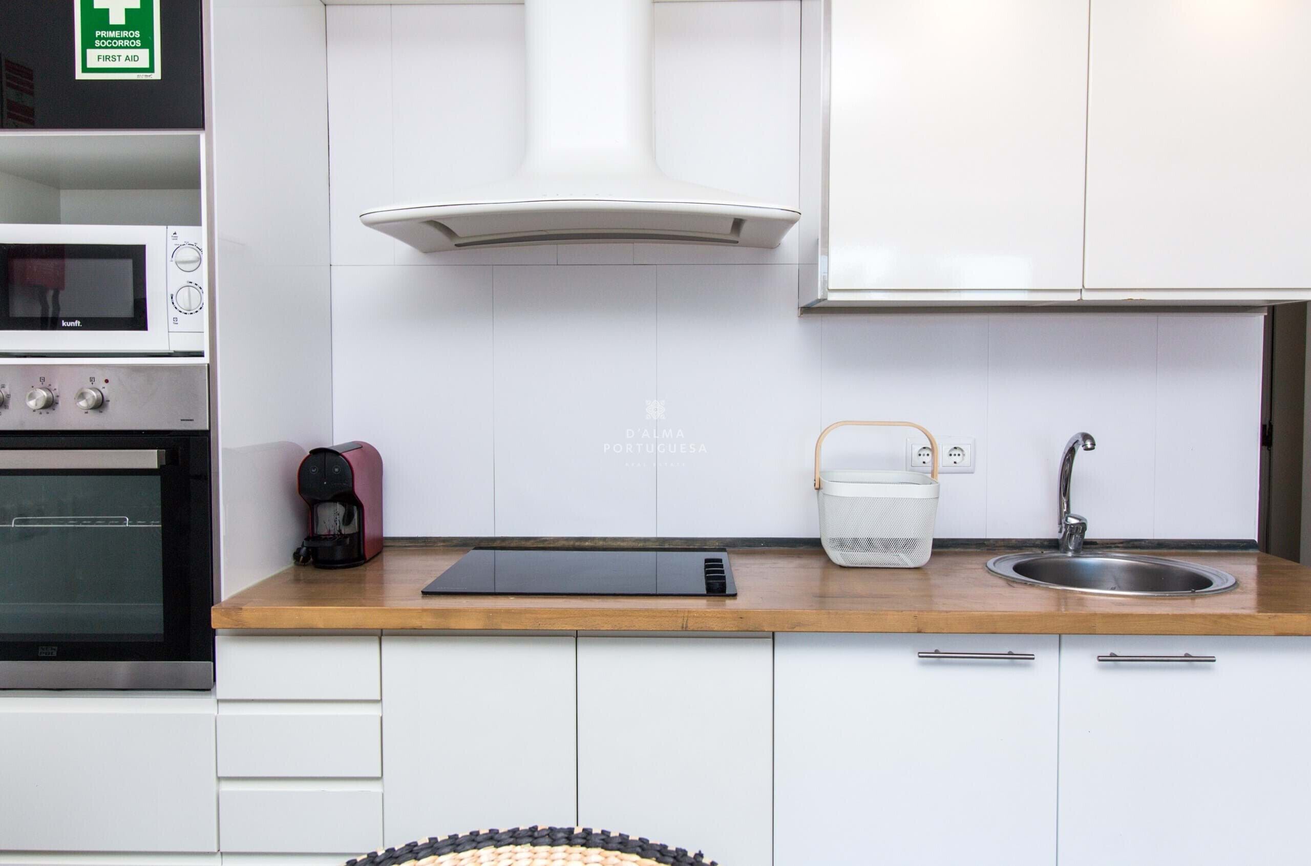 A kitchen with white cabinets, a stainless steel sink, a coffee maker, and a microwave.