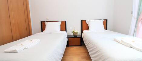 A hotel room with two beds, wooden flooring, and a nightstand with a vase.
