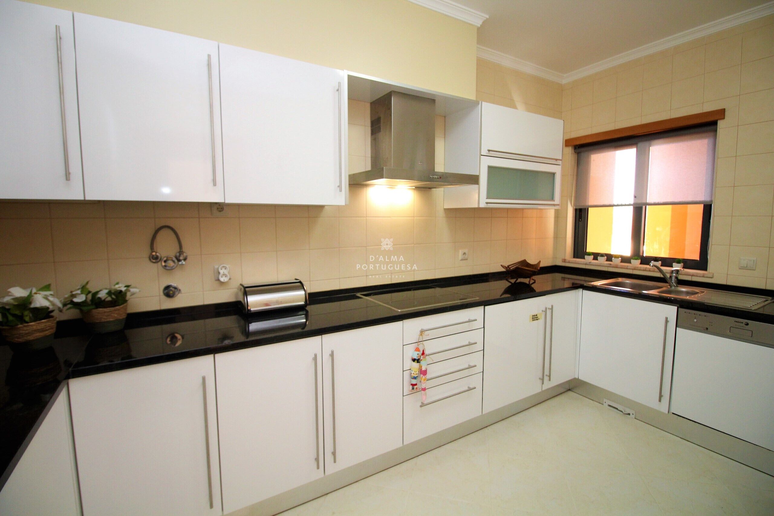 A kitchen with white cabinets, a stainless steel range hood, a microwave, and a window with blinds.