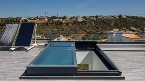 A rooftop terrace with solar panels, a glass balustrade, and a view of a hillside residential area. - Dalma- Villa da Ourada (Albufeira)