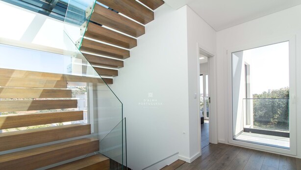 A modern staircase with glass railings, wooden steps, and a white wall with a logo. - Dalma- Villa da Ourada (Albufeira)