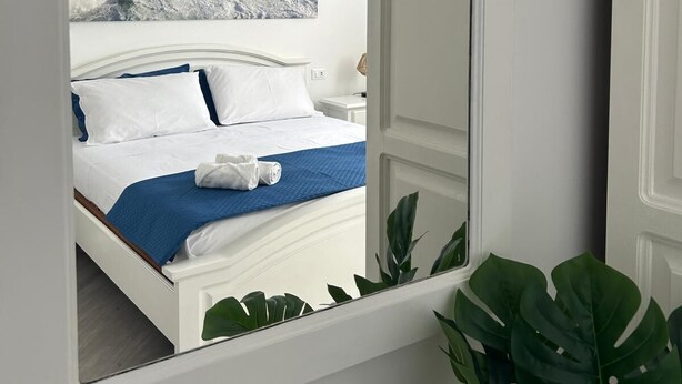 Een slaapkamer met een bed, nachtkastje, lamp en een grote spiegel.