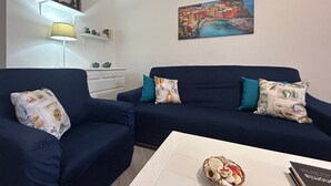 Een woonkamer met twee donkerblauwe banken, een witte salontafel en een schilderij van een kustplaatsje.