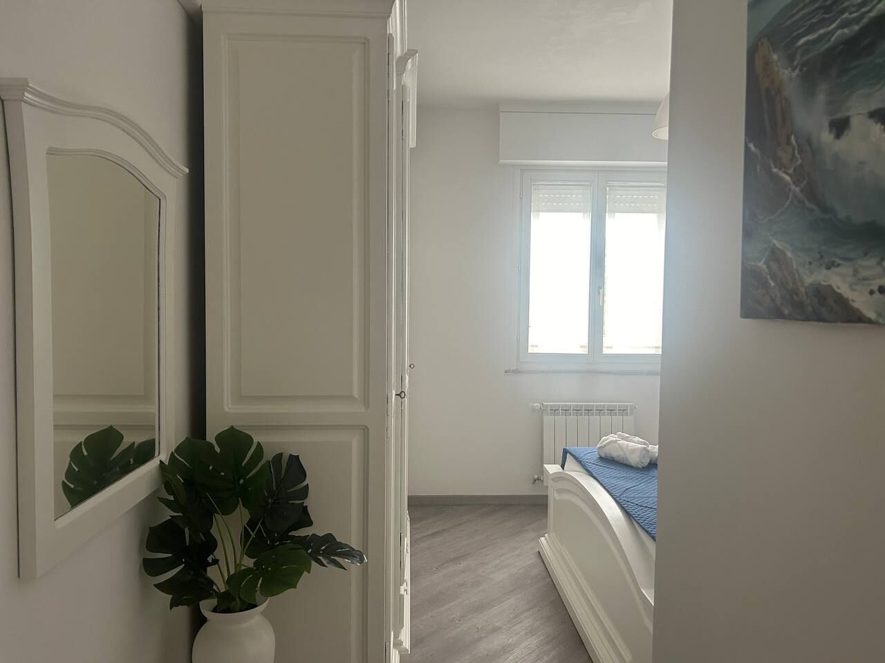 A bedroom with a bed, a radiator, a window, and a plant.