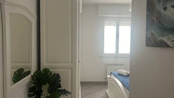 A bedroom with a bed, a radiator, a window, and a plant.