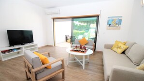 Una sala de estar con televisor, sofá, sillón, mesa y puerta corrediza de vidrio que da a un balcón.