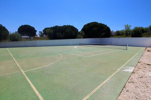 Ein Tennisplatz im Freien mit Netz, umgeben von Bäumen und blauem Himmel.