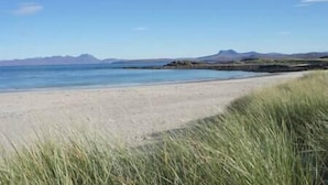 Une plage avec un ciel dégagé et des montagnes à l’horizon.