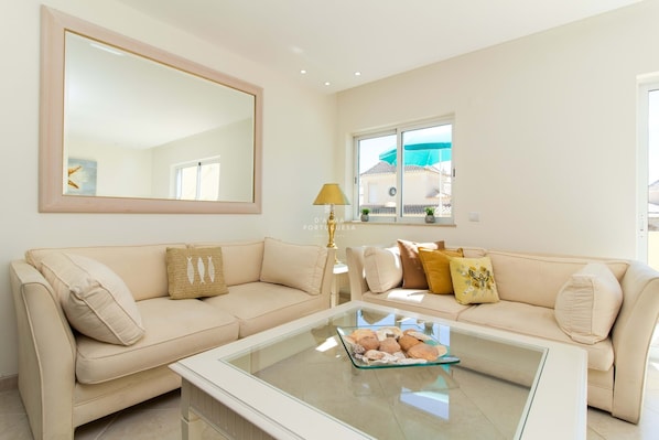 A living room with a beige sofa, a glass coffee table, and a large mirror.