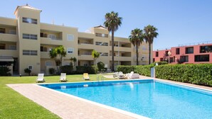 Una piscina con lettini, un prato ben curato e un edificio a più piani con balconi.