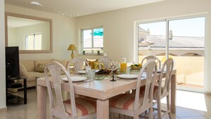 Zona pranzo con tavolo imbandito per quattro persone, divano, televisore e balcone con vista.