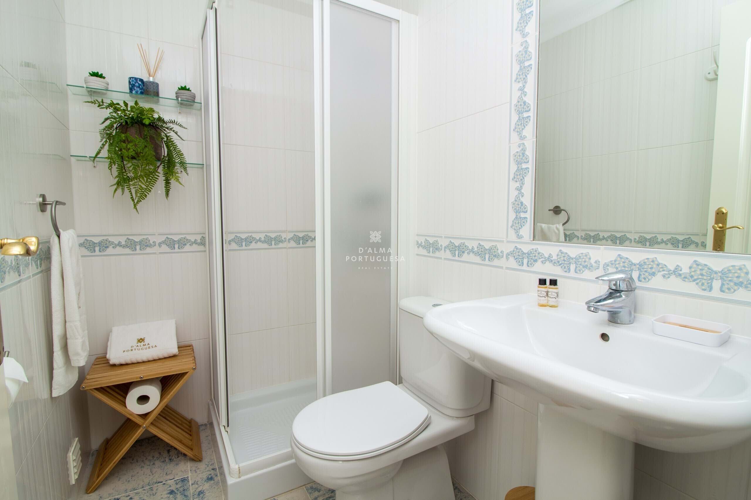A bathroom with a toilet, sink, shower, and a towel rack with a plant.