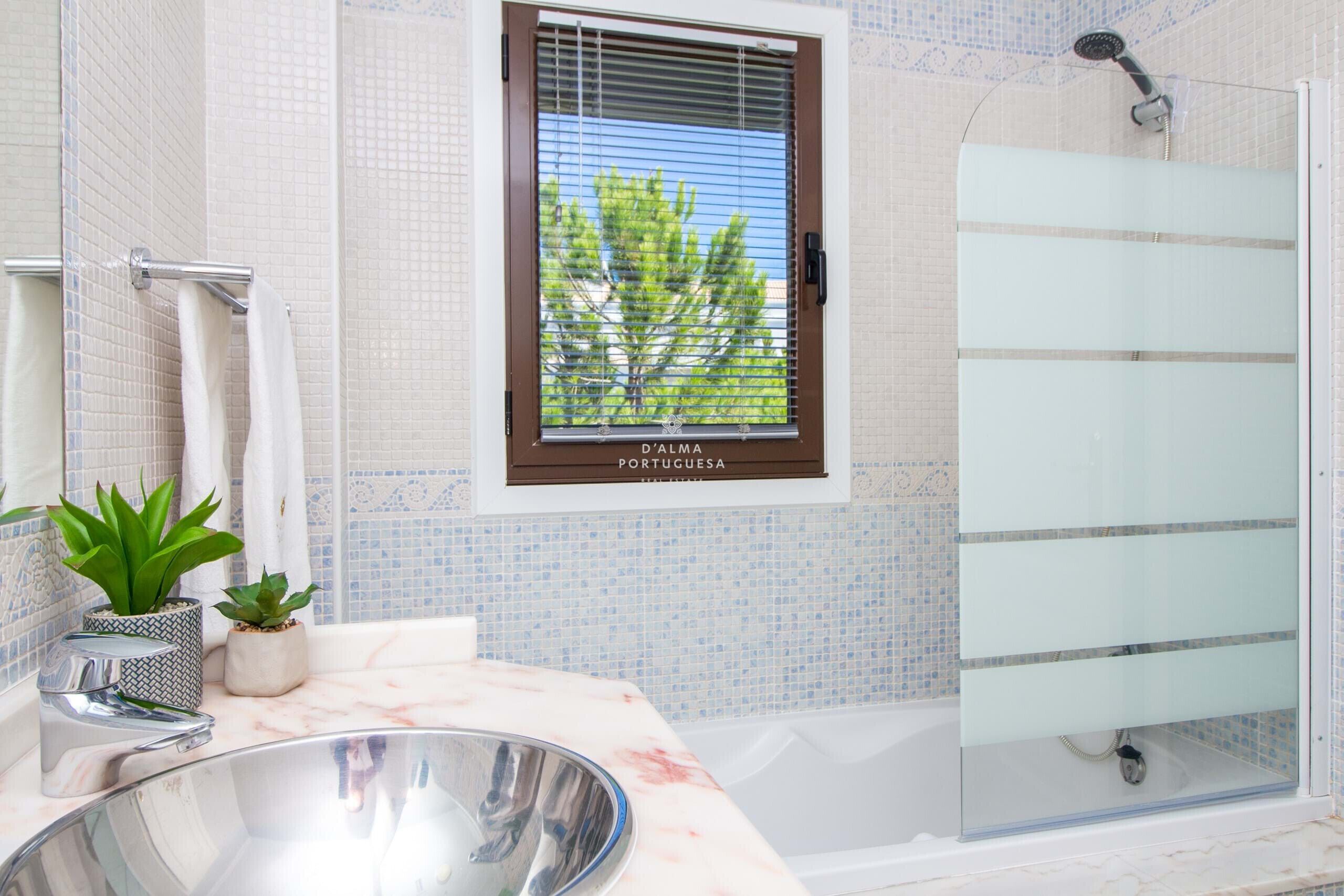 A bathroom with a shower, a sink with a large basin, and a window with a view of trees.