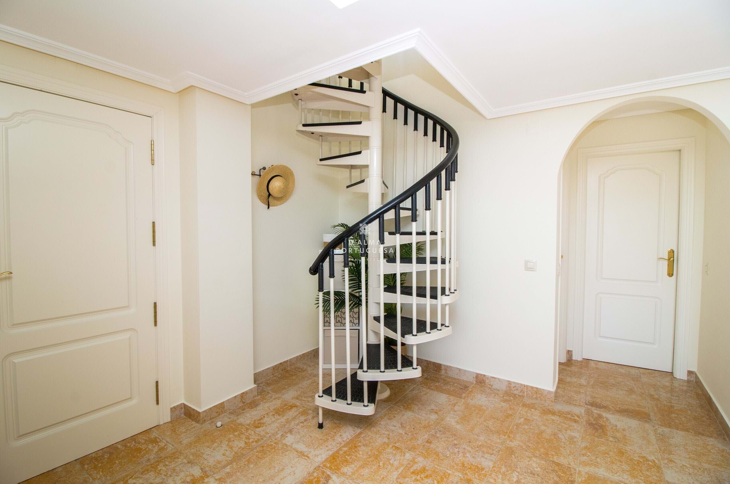 A spiral staircase with white railings and black handrails, leading to an upper floor.