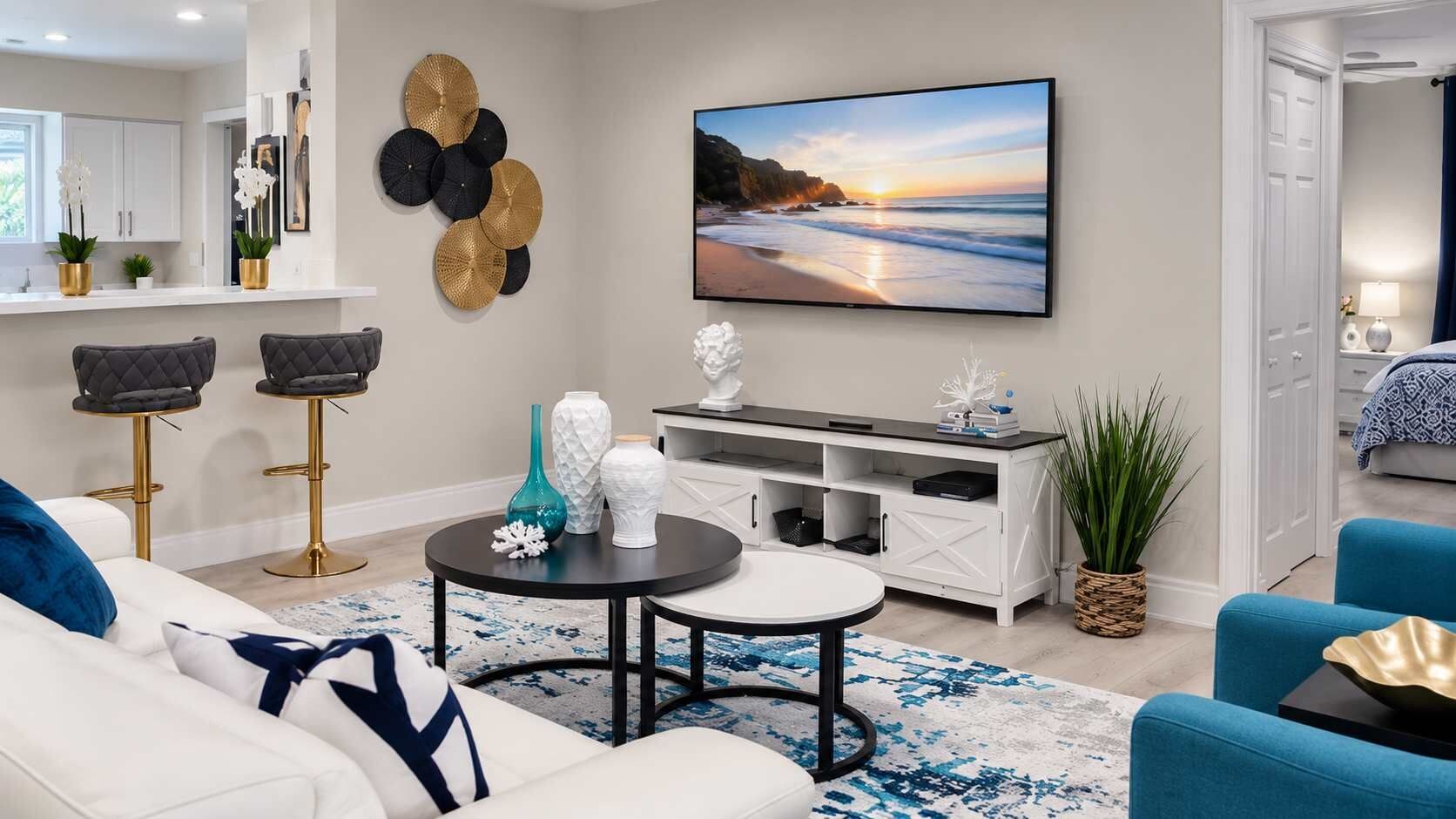 A modern living room with a flat-screen TV, two bar stools, a white sofa, and a blue armchair.
