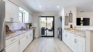 A modern kitchen with white cabinets, a granite countertop, and a sliding glass door leading to a balcony. - Naples Gem Near Beach | Heated Pool & BBQ (Naples)