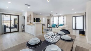 A modern living space with a dining area, kitchen, and a balcony with outdoor furniture. - Naples Gem Near Beach | Heated Pool & BBQ (Naples)