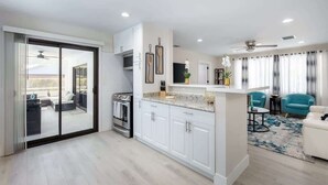 A modern kitchen with white cabinets, a central island, and a dining area with teal chairs. - Naples Gem Near Beach | Heated Pool & BBQ (Naples)