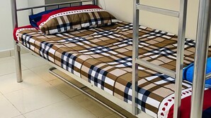 Una cama litera con estructura metálica, un edredón estampado y un almohadón con diseño a cuadros.