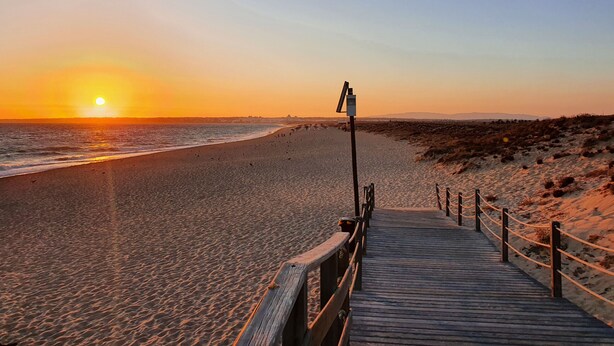 A wooden boardwalk leading to a beach with a sunset in the background. - Apartamento do Pinhal D'alma Portuguesa (Albufeira)