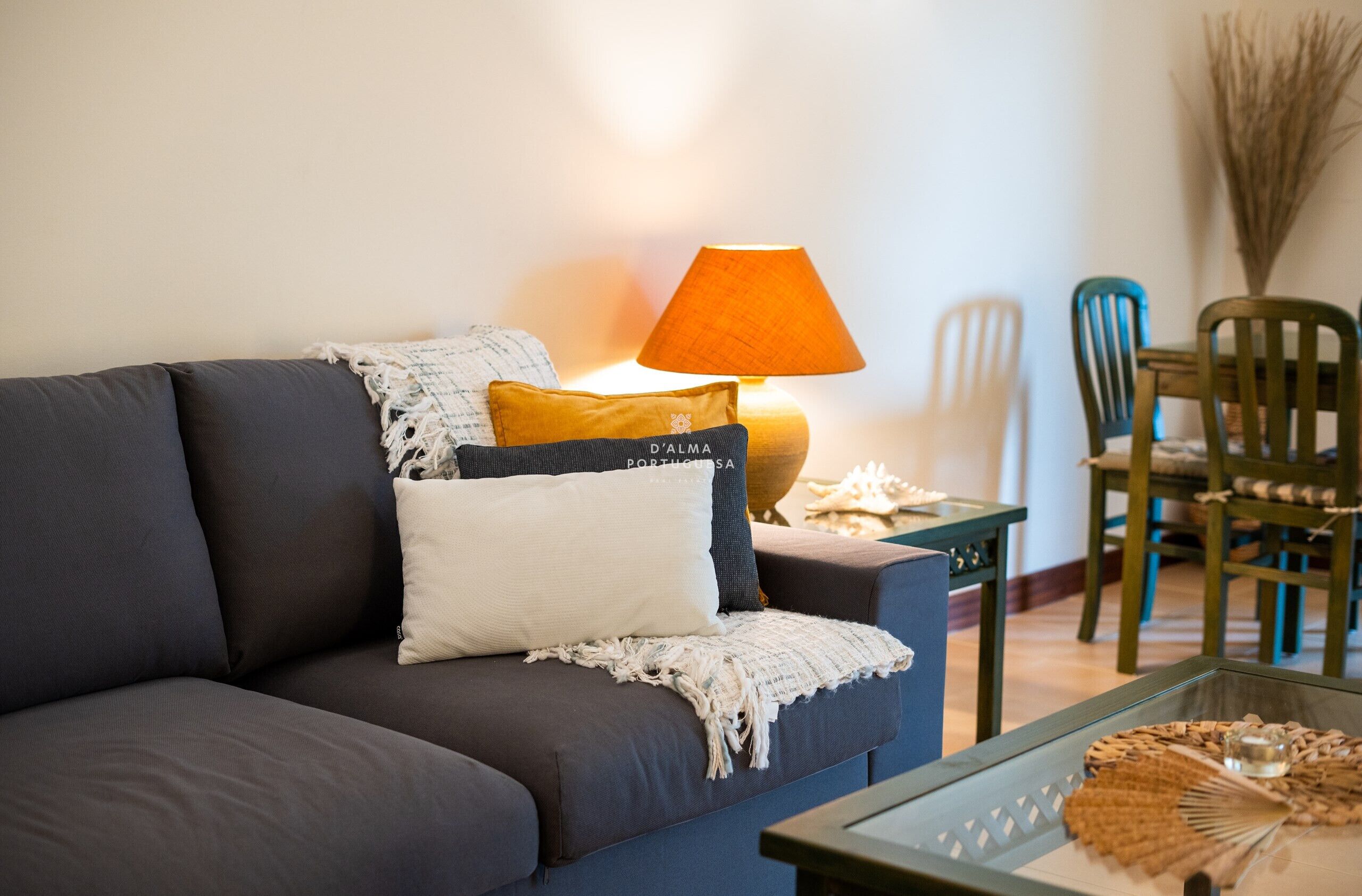 A living room with a dark sofa, a table with a woven placemat, and a lamp with a beige shade.
