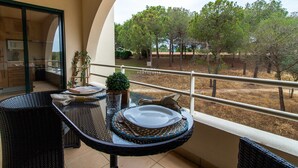 A balcony with a dining table set for two, a small potted plant, and a view of trees and a building in the distance. - Apartamento do Pinhal D'alma Portuguesa (Albufeira)