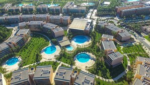 Un complejo turístico con múltiples piscinas dispuestas en un diseño circular, rodeado de exuberante vegetación y edificios modernos.