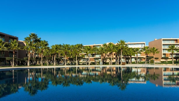 Un hotel con piscina que refleja palmeras y edificios.