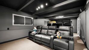 A home theater room with black leather recliners, a large flat-screen TV, and plush toys on the seats.