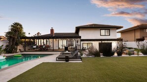 A modern house with a swimming pool, outdoor seating, and a well-maintained lawn.