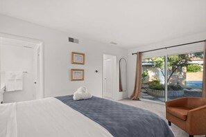 Une chambre à coucher comprenant un lit, une chaise, une porte-fenêtre coulissante donnant sur un patio, et deux tableaux encadrés accrochés au mur.