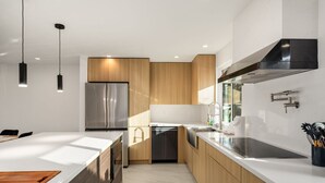 Une cuisine moderne dotée d’un îlot central, d’appareils électroménagers en acier inoxydable, de meubles en bois et de luminaires suspendus.